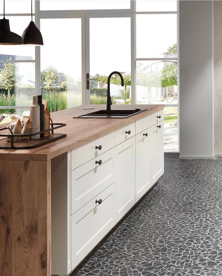 Kitchen island with light wood countertop, white cabinets, black faucet, and patterned floor.