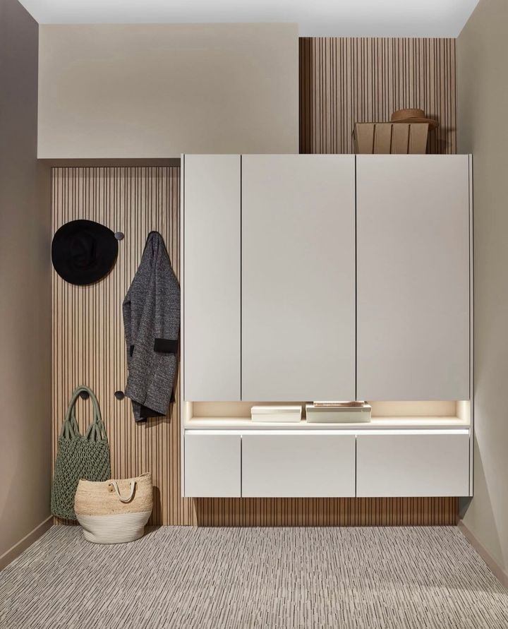 Hallway storage with coat, bag, and hat. Light beige cabinets, wooden paneling, and a patterned rug.