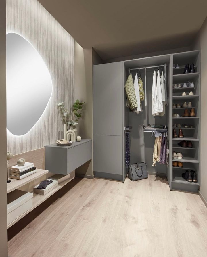 Gray walk-in closet with clothing racks, shoe shelves, and a large mirror. Light wood floor and neutral walls.