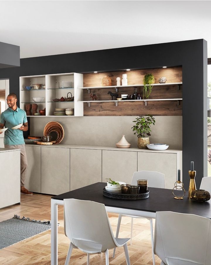 Modern kitchen with a man, cabinets, shelves, dark table, and chairs.
