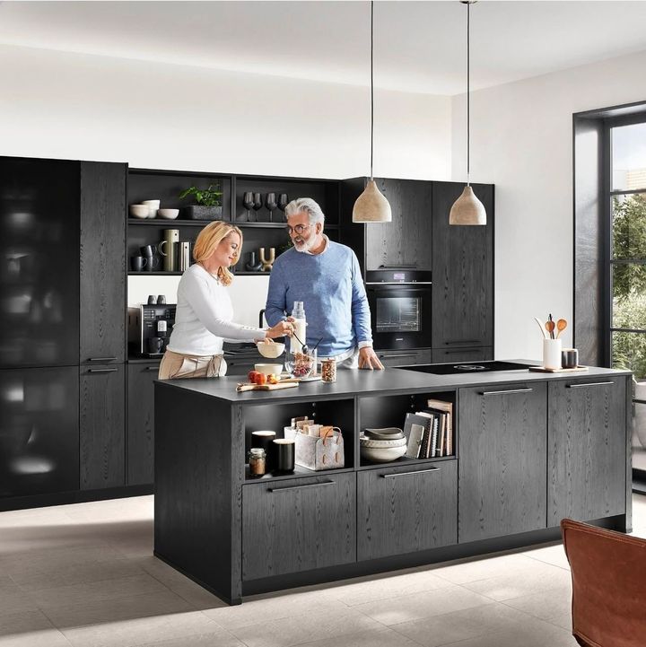 Mature couple in modern black kitchen, preparing food.