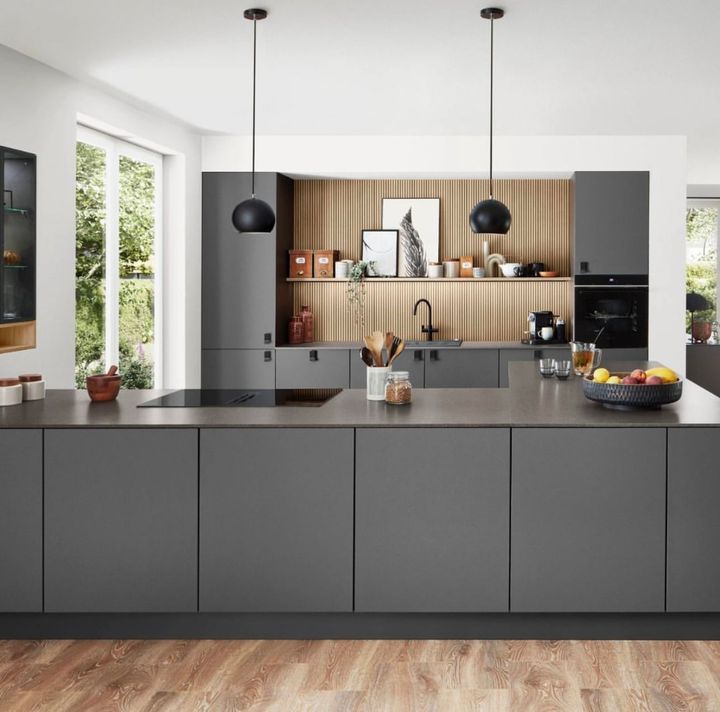 Modern gray kitchen with island, wood floor, black pendant lights, and window view.