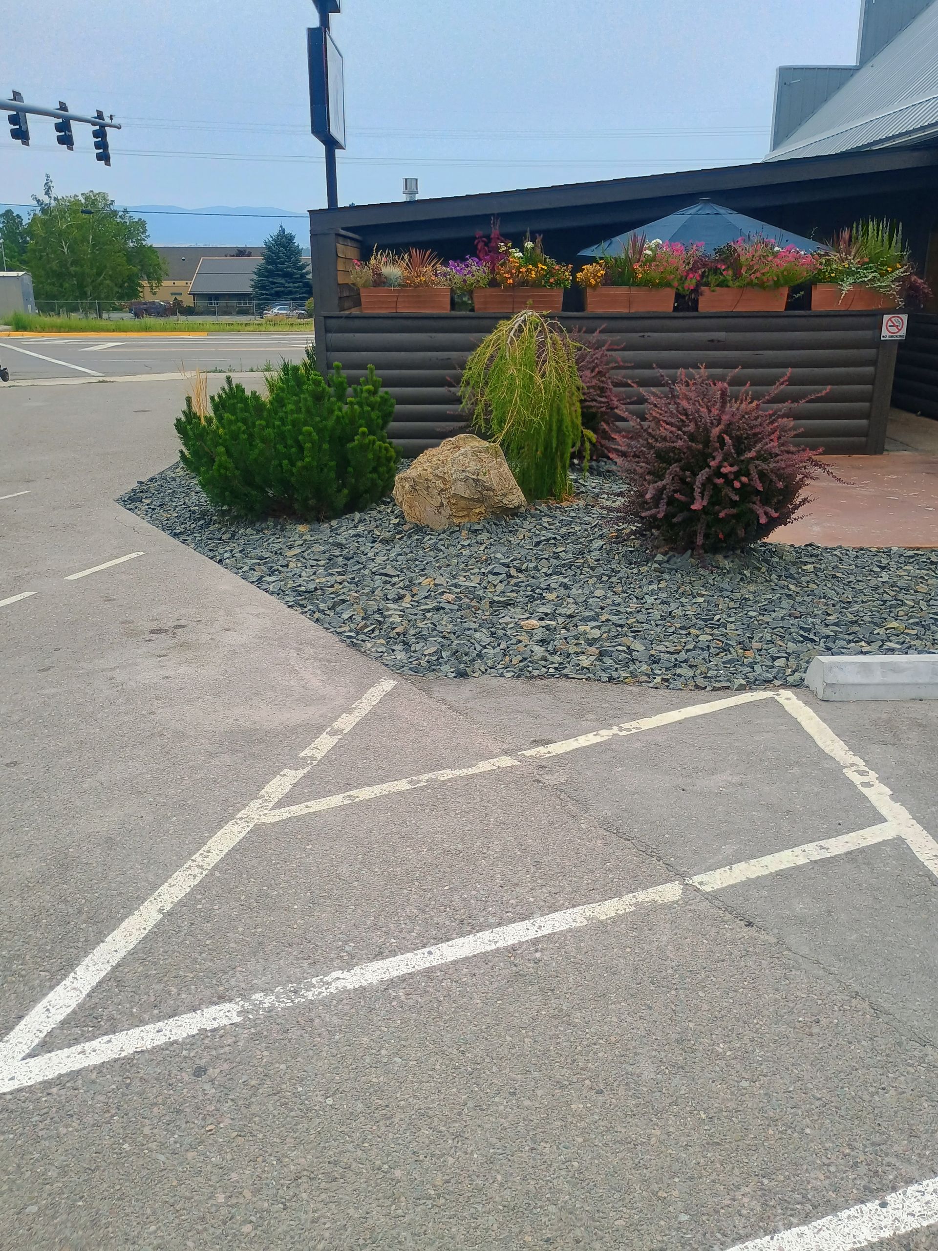 Parking area with landscaping: green bushes, rock bed, and floral planters next to a building.