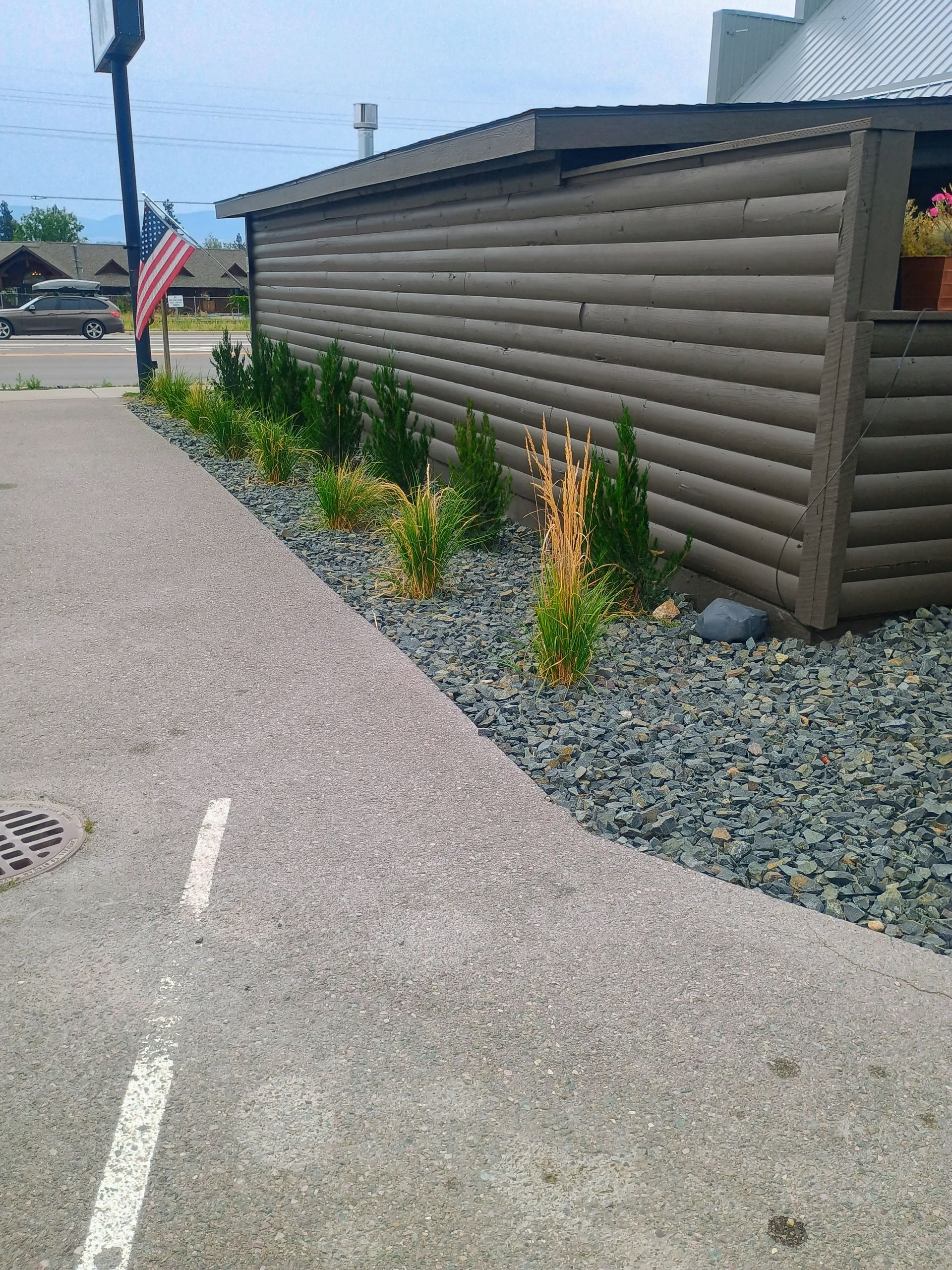 Sidewalk next to a building with a garden bed of greenery and dark rocks.