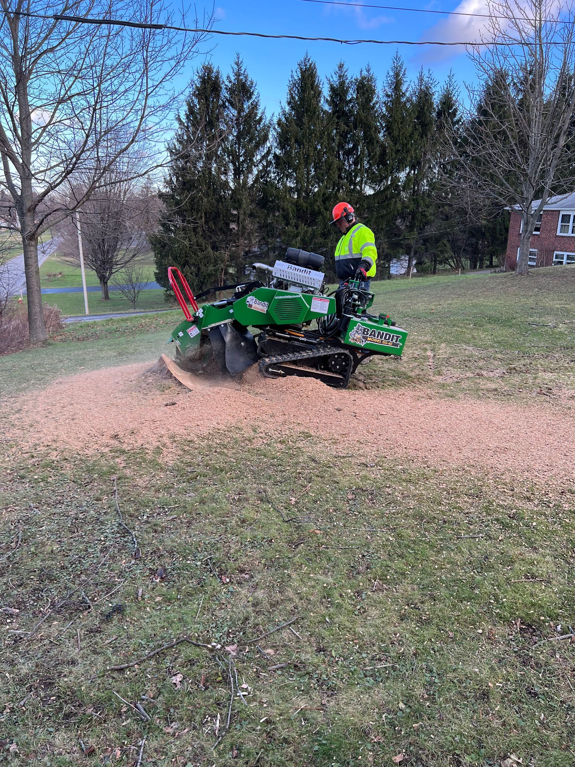 A man is using a stump grinder to remove a tree stump in a field.