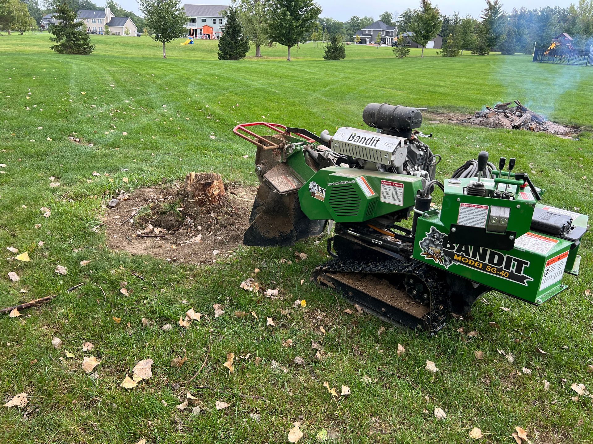A green stump grinder is sitting in the grass next to a tree stump.
