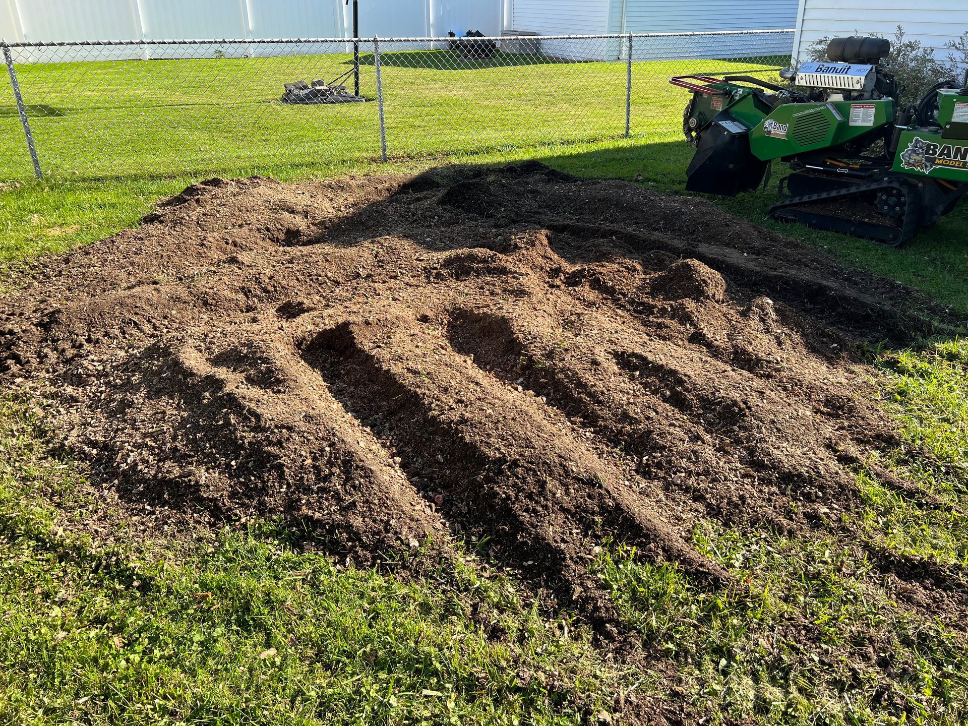 A stump grinder is sitting next to a pile of dirt in the grass.