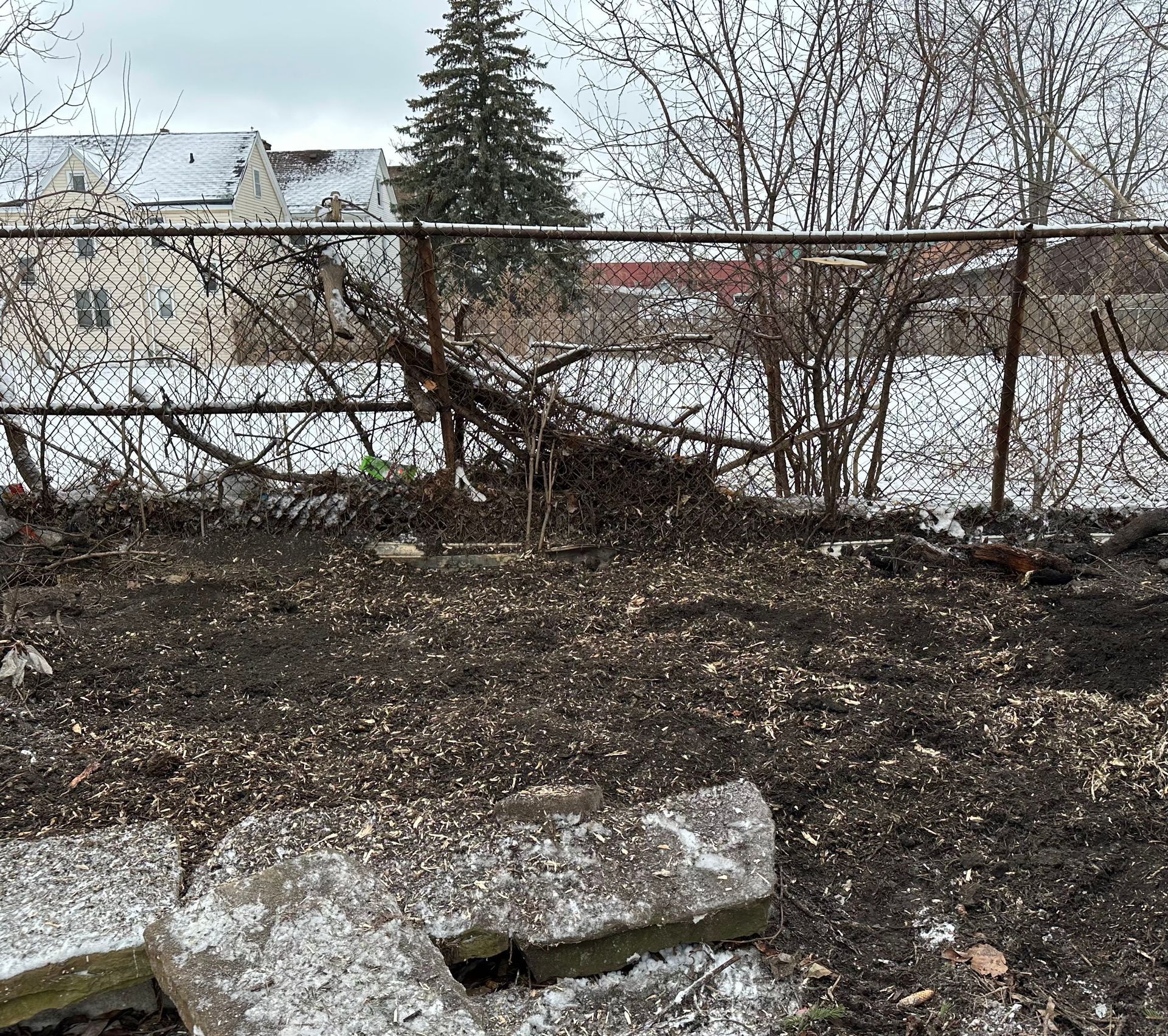 A chain link fence is surrounded by a pile of dirt and trees.