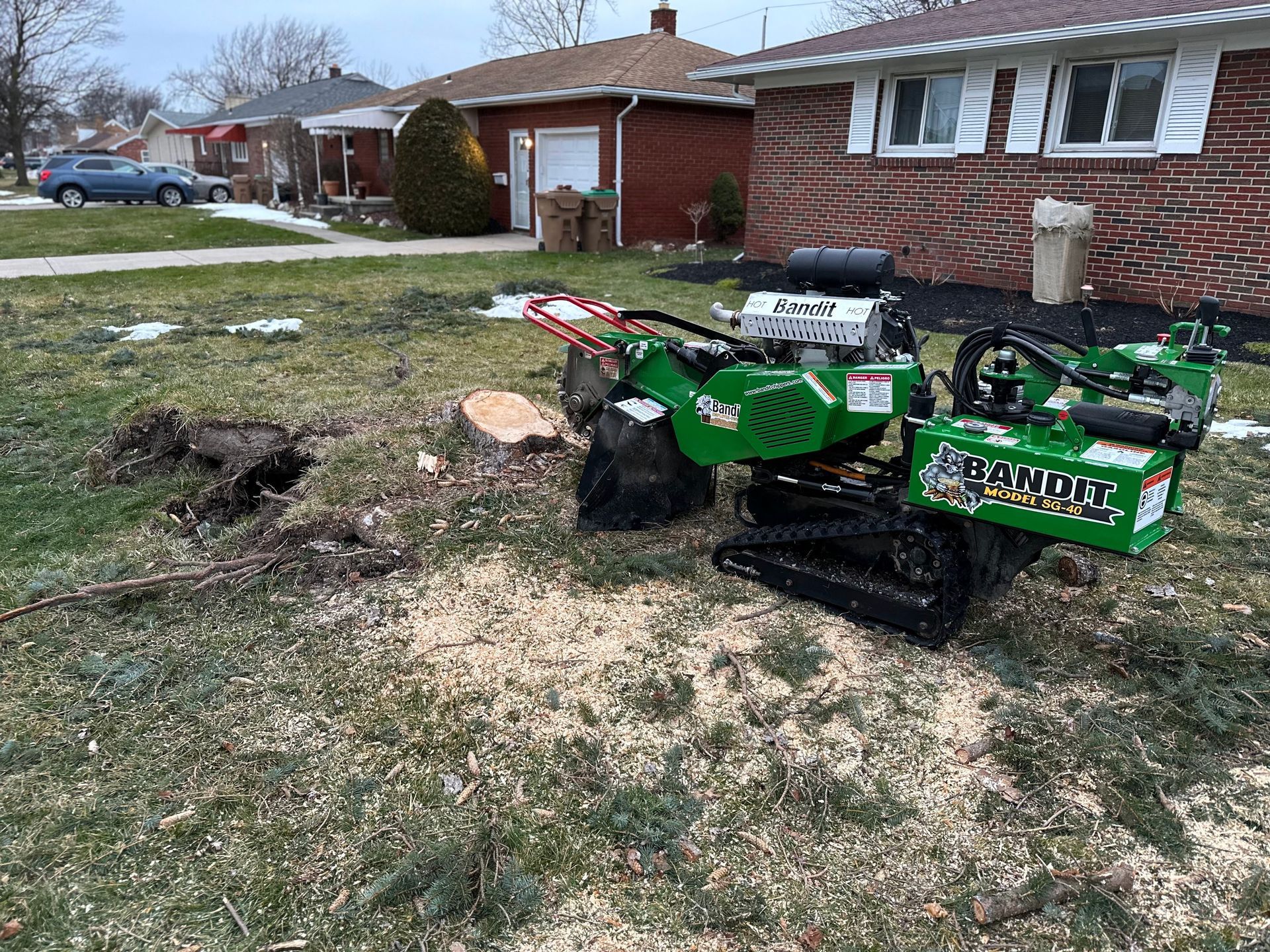A green stump grinder is sitting in the grass in front of a house.