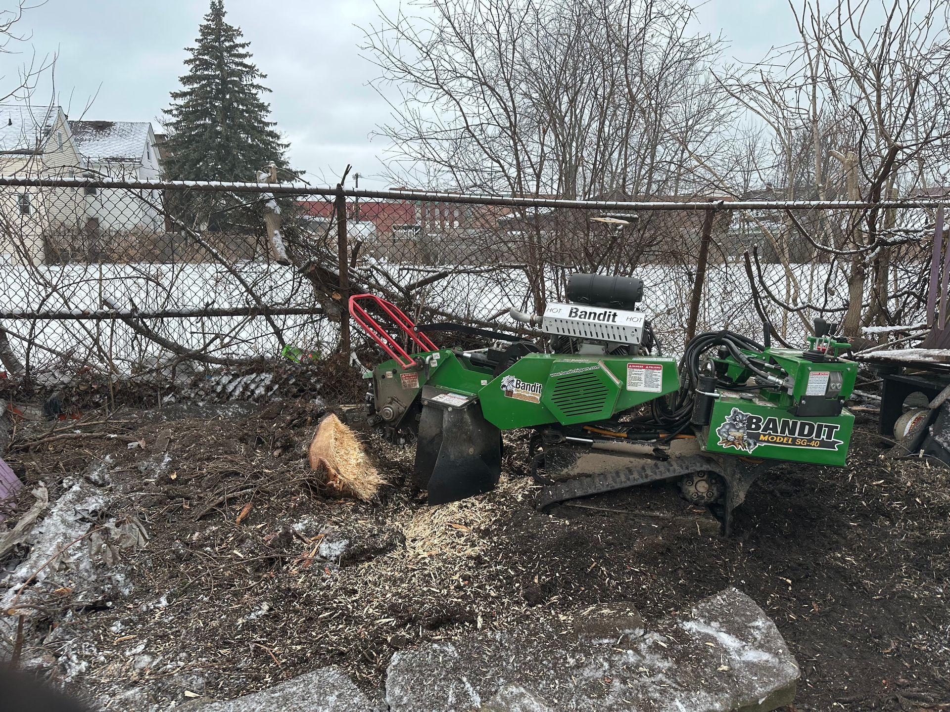 A green stump grinder is sitting in a yard next to a fence.