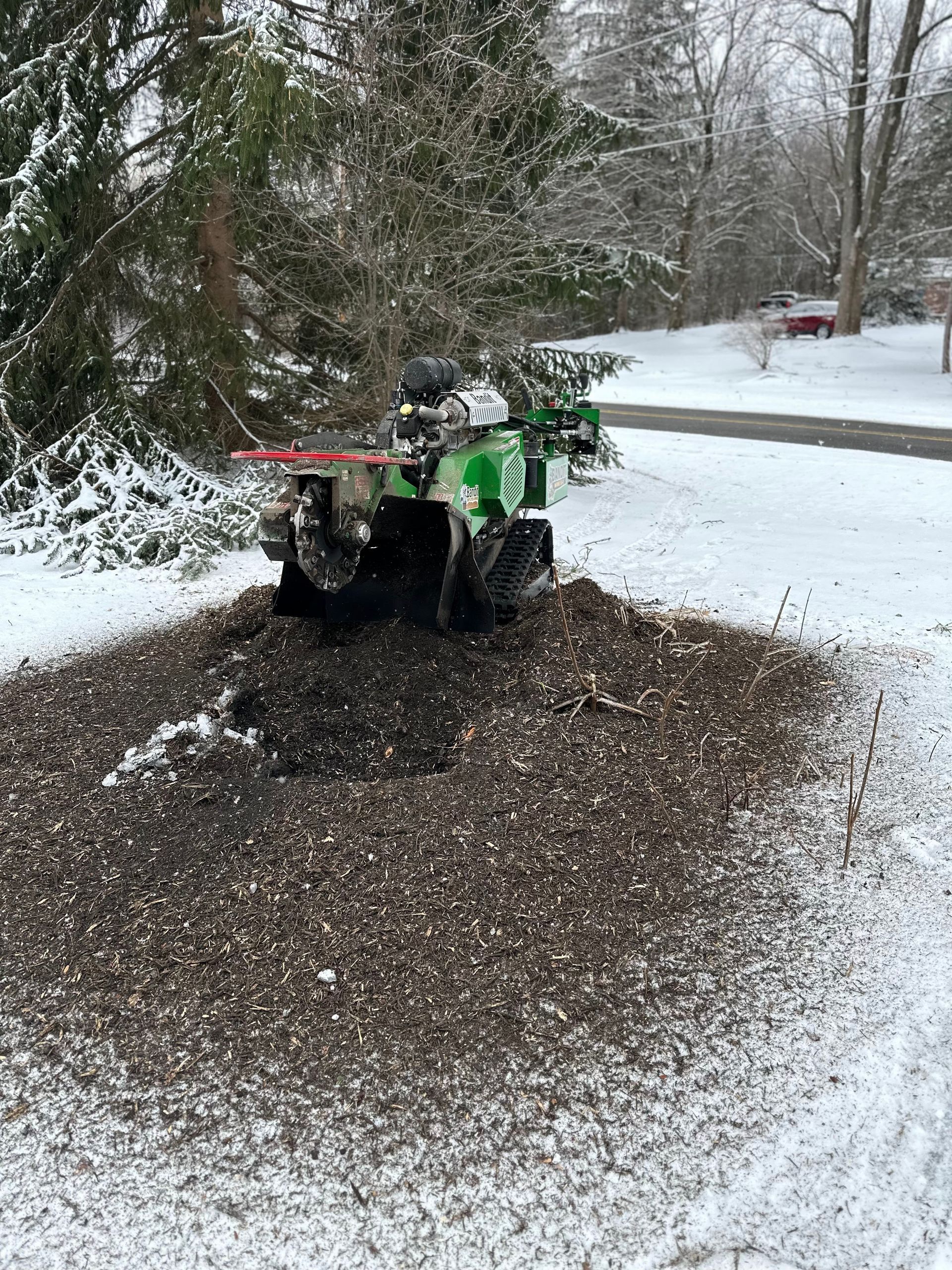 A green atv is stump grinding a tree in the snow.