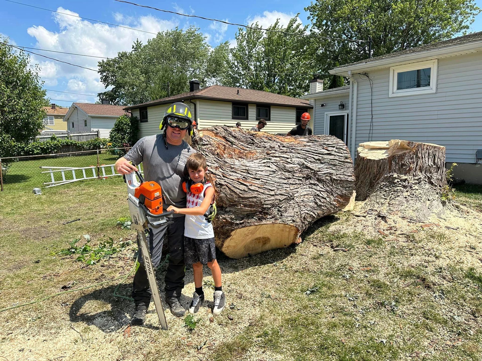 A man and a boy are standing next to a large tree stump.