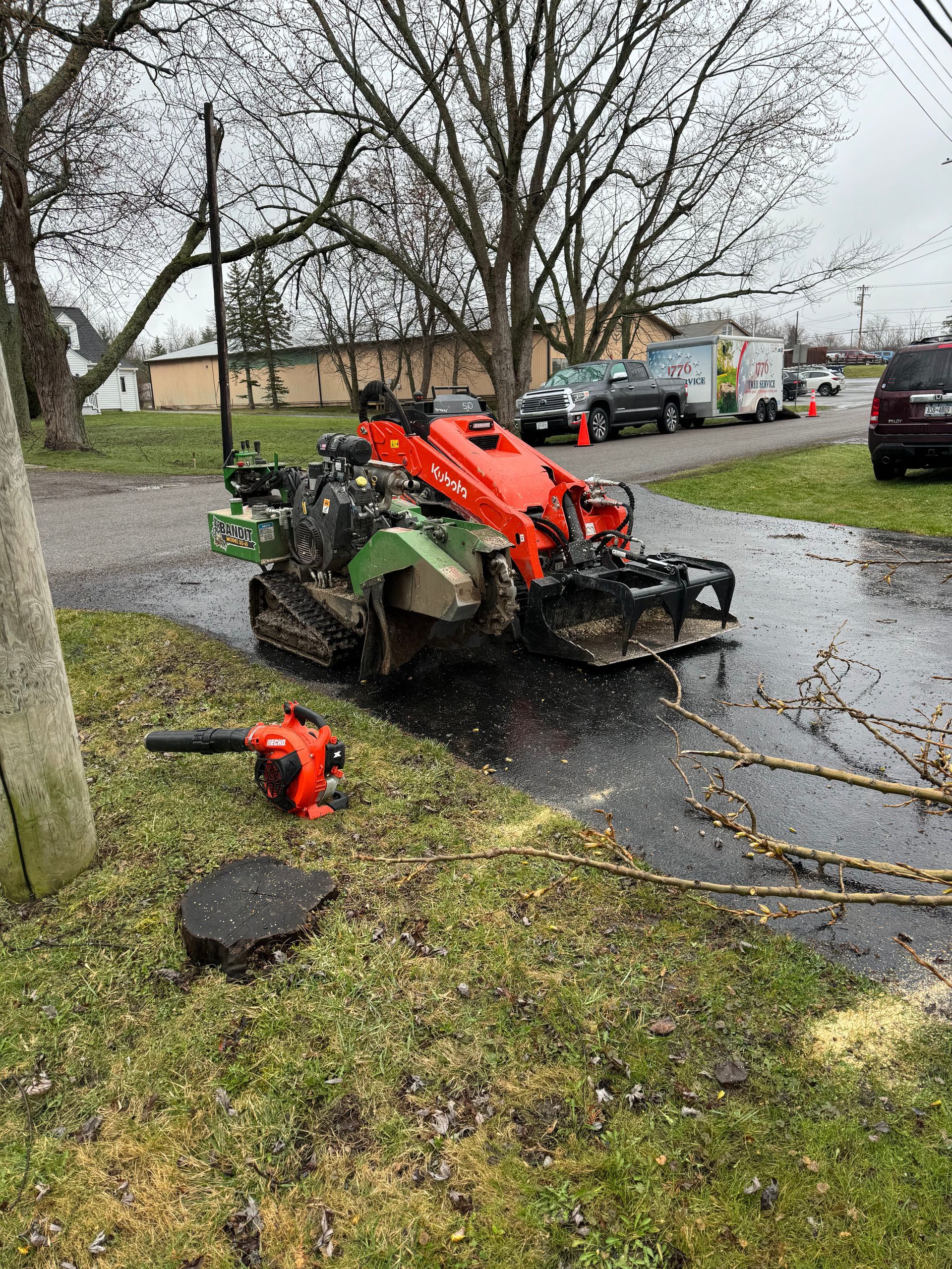 A stump grinder is sitting on the side of the road next to a blower.