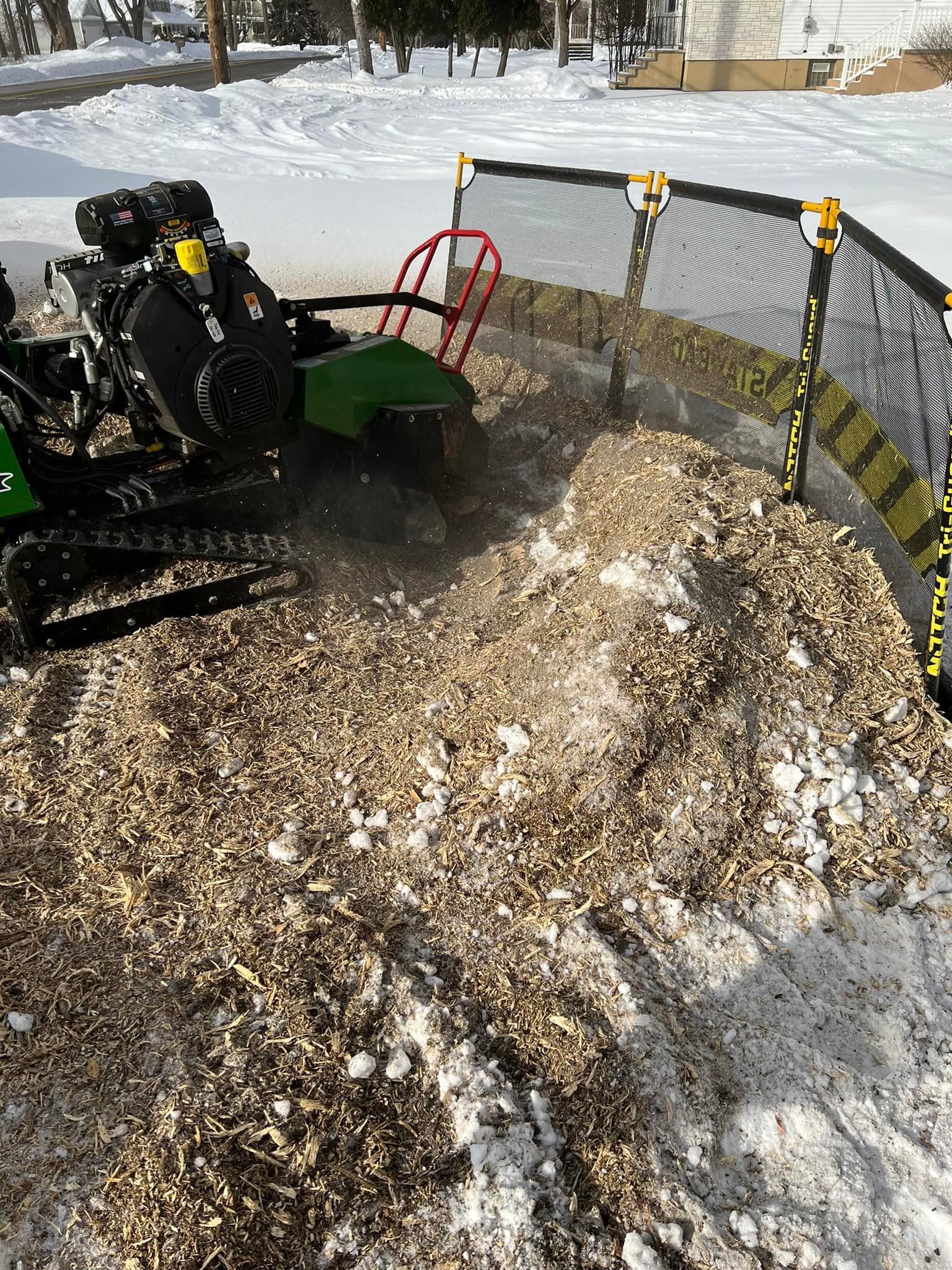 A stump grinder is cutting a tree stump in the snow.