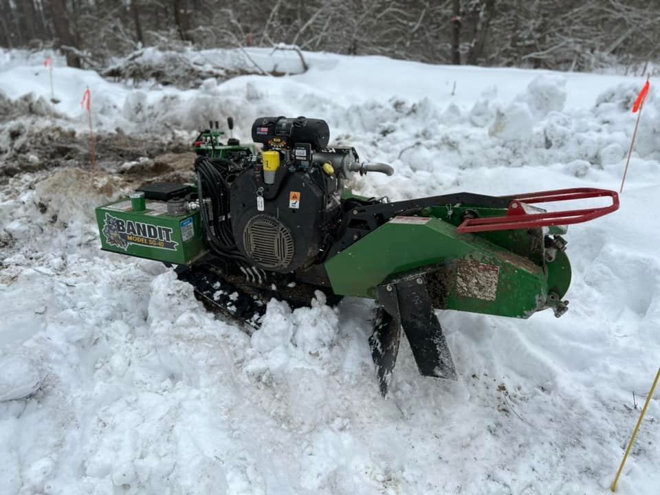A green stump grinder is sitting in the snow.