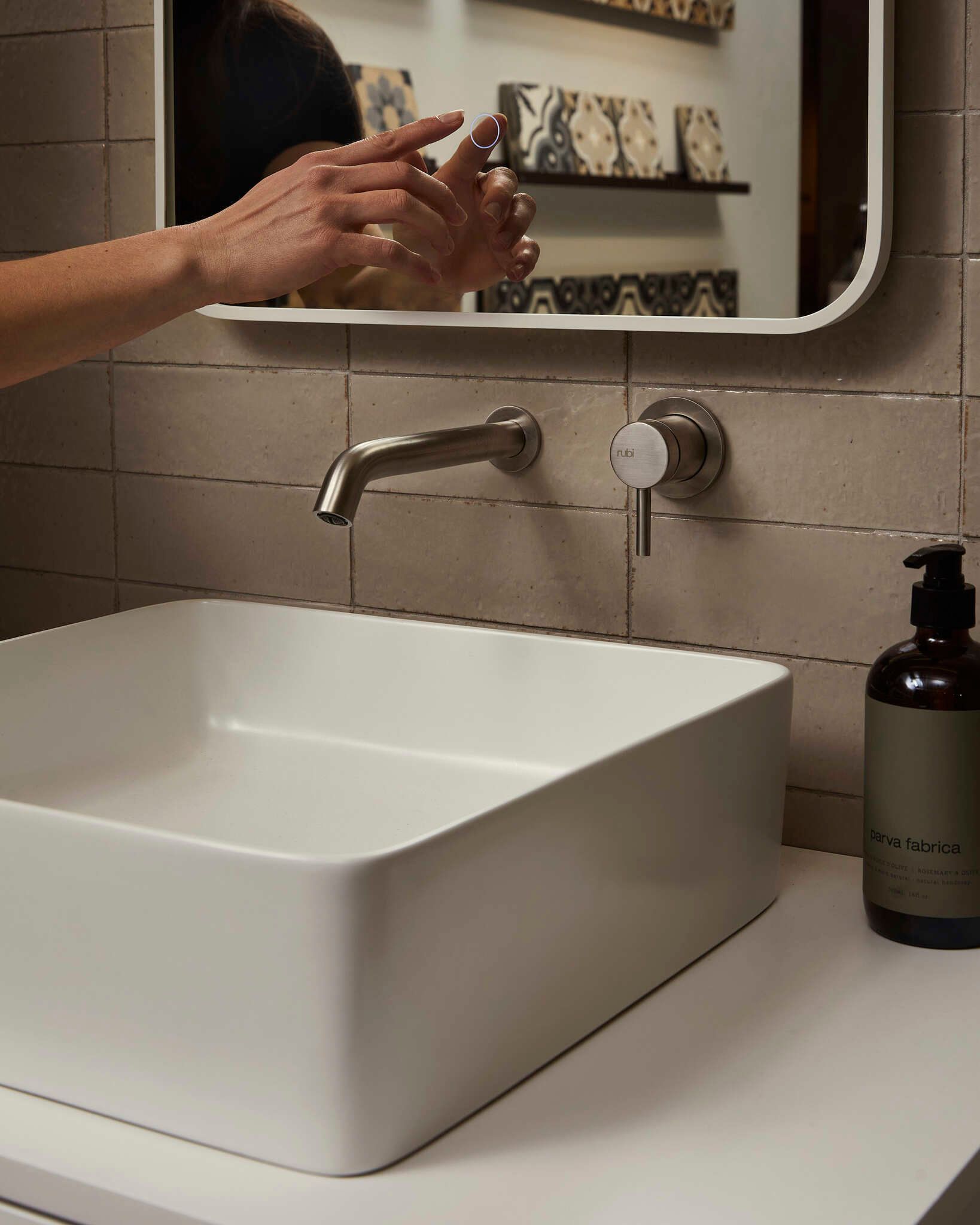 Une personne se lave les mains devant un lavabo carré blanc moderne. Robinet en métal brossé, distributeur de savon et miroir.