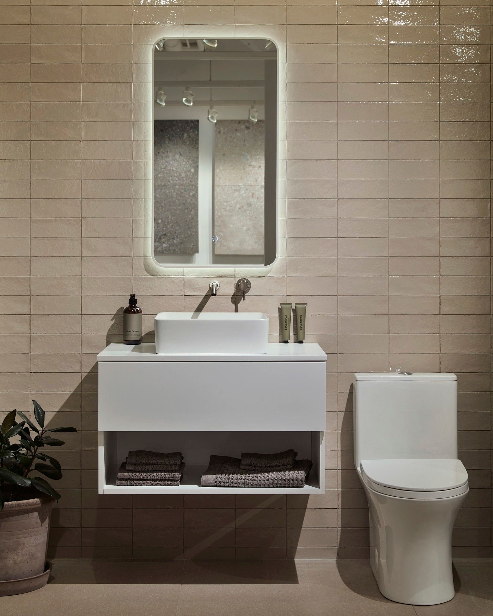 Salle de bain blanche moderne avec vanité flottante, miroir éclairé et toilettes ; fond de carrelage neutre.