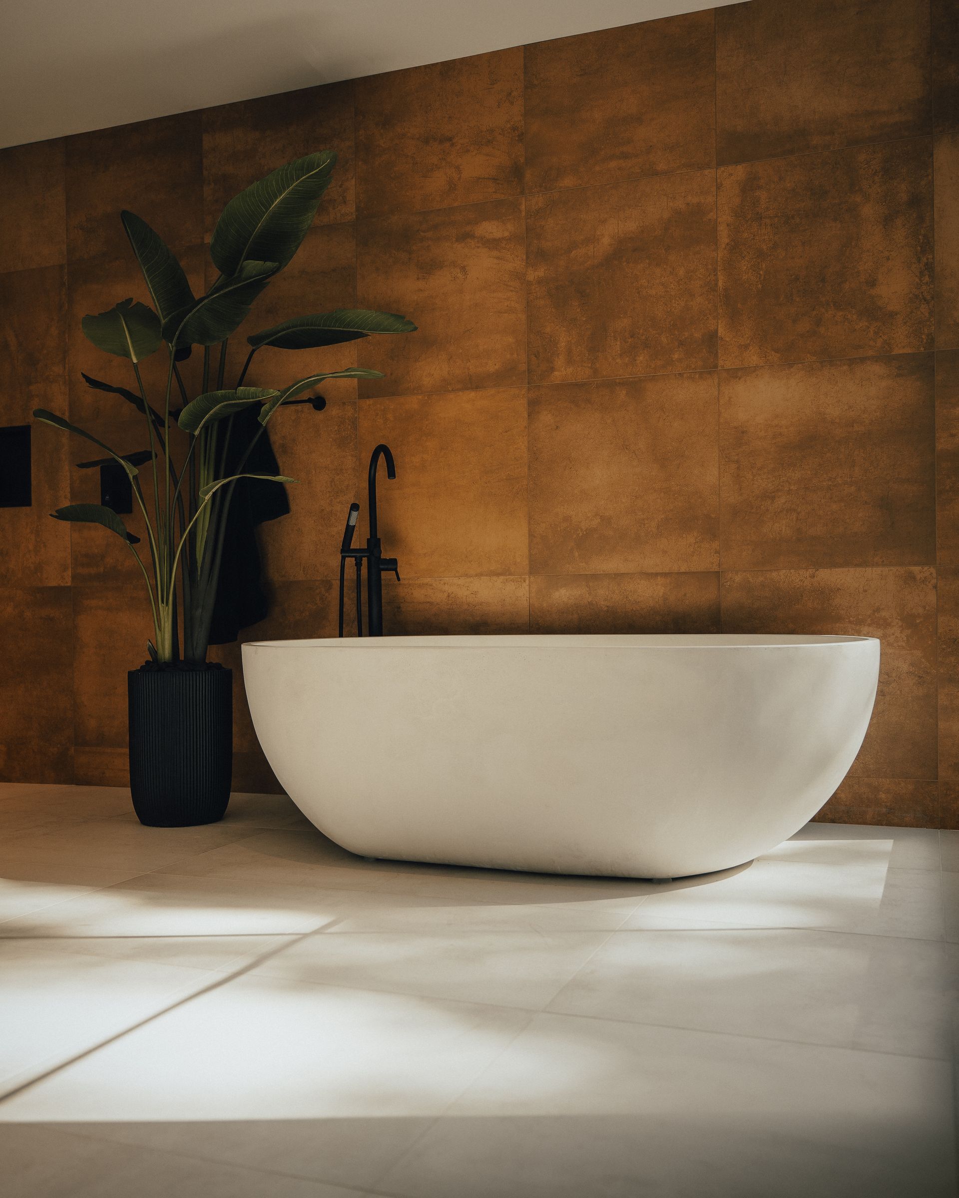 Baignoire blanche dans une salle de bain moderne avec mur en carrelage marron et plante.
