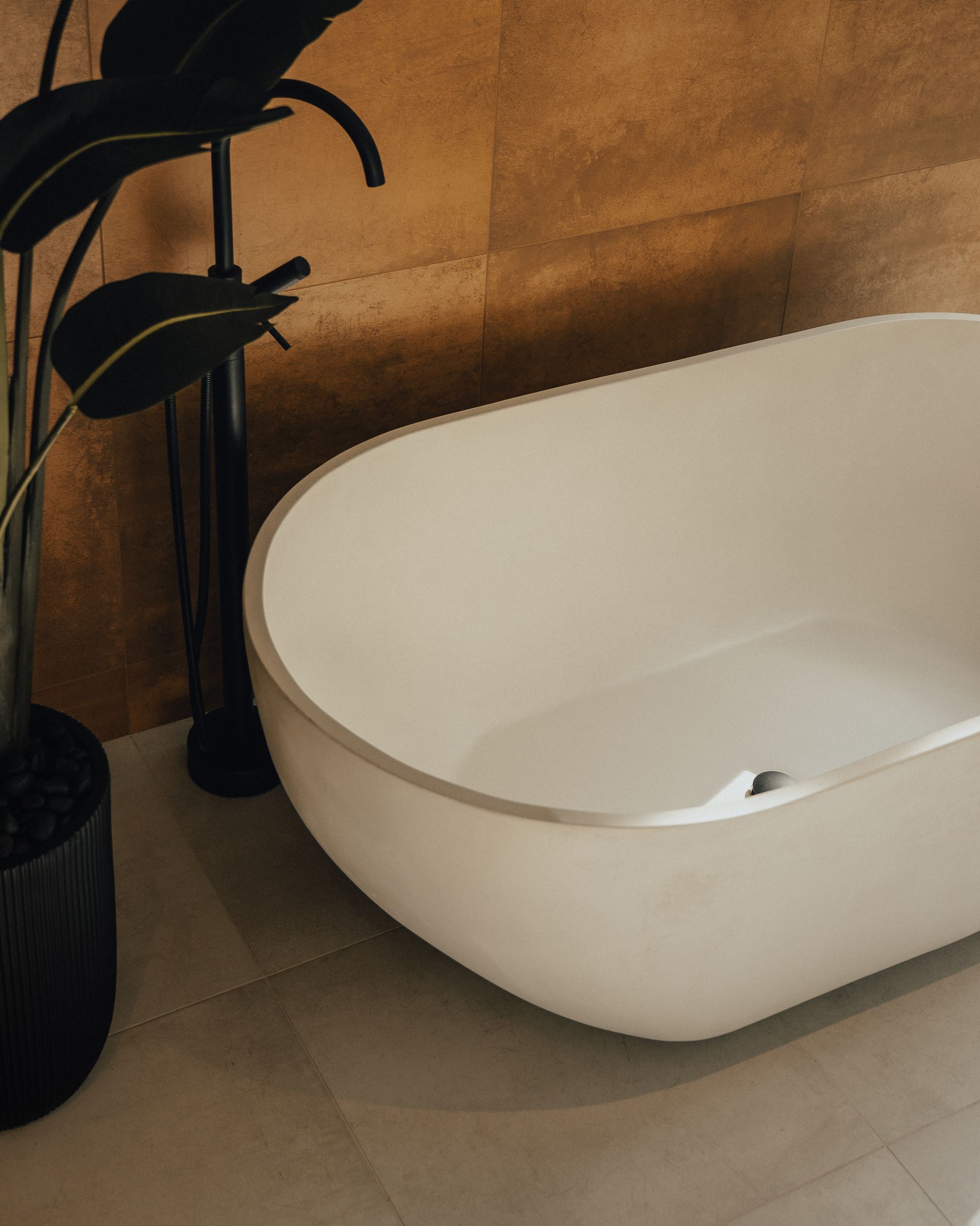 Baignoire ovale blanche dans une salle de bain moderne avec plante et mur aux tons dorés.