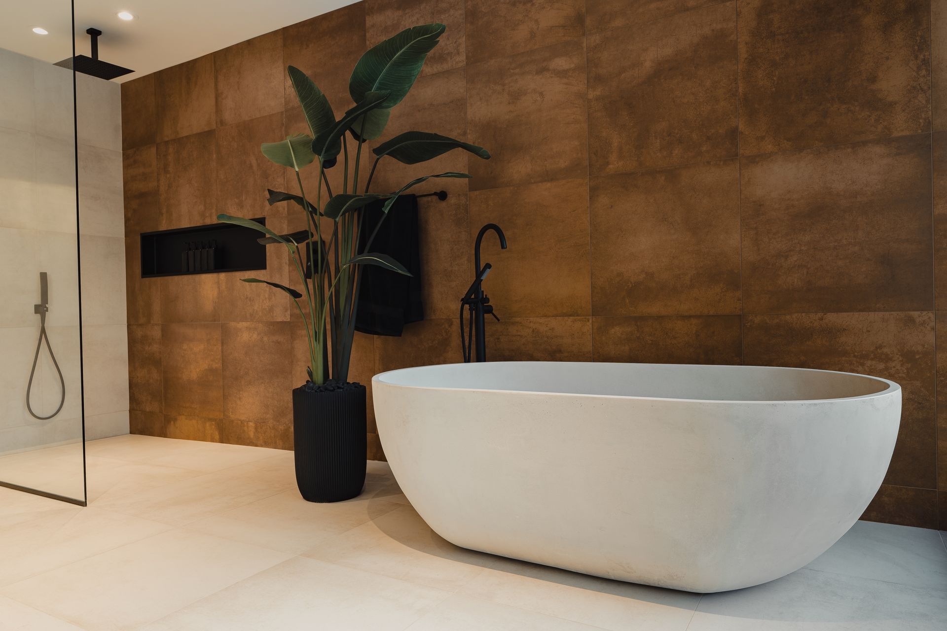 Salle de bain moderne avec baignoire blanche, mur en bronze et une grande plante.