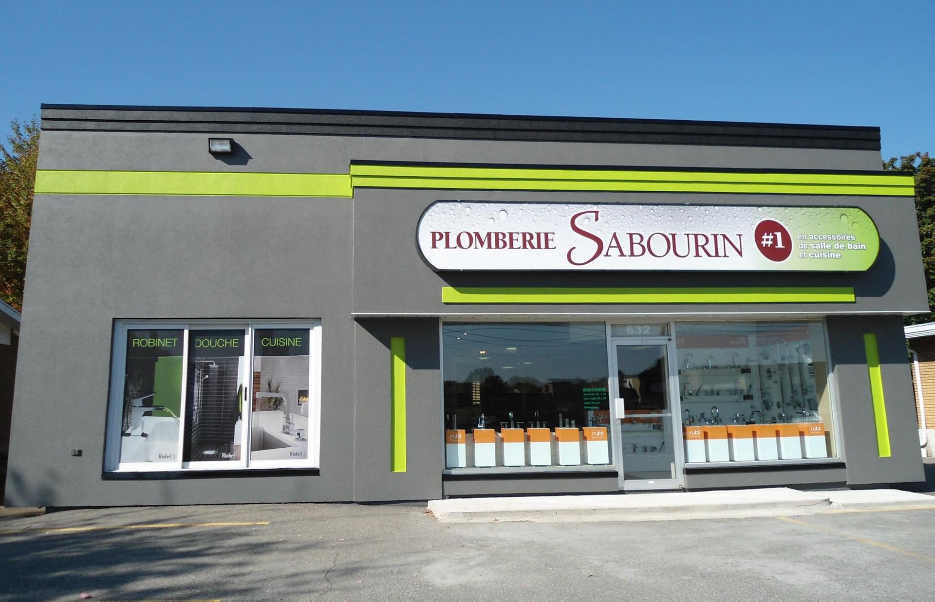 Vitrine de la Plomberie Sabourin. Bâtiment gris avec boiseries, fenêtres et enseignes vertes.
