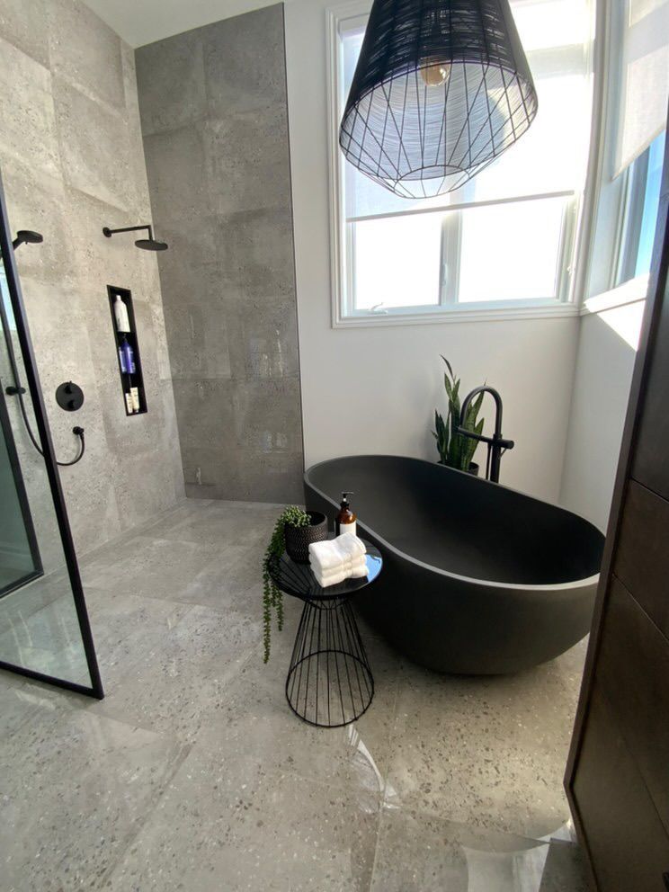 Salle de bain moderne avec carrelage gris, baignoire noire et luminaires noirs.