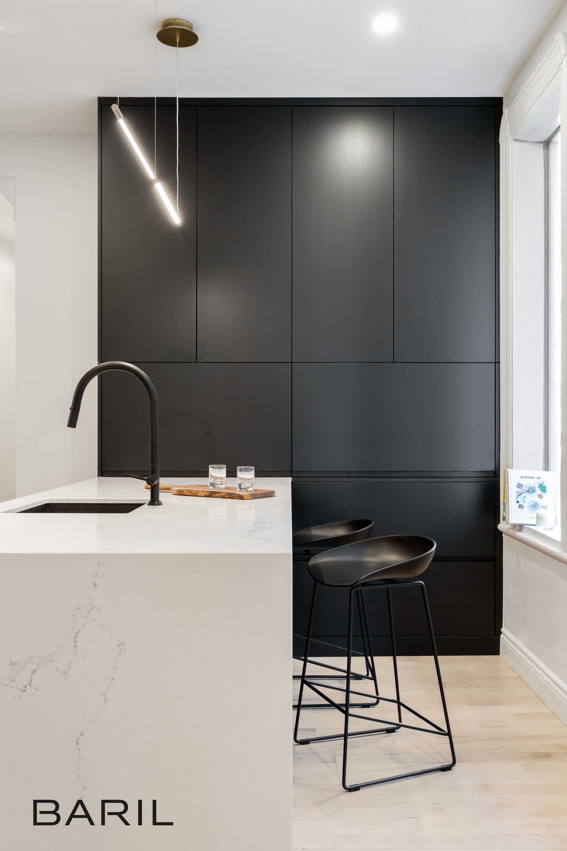 Cuisine moderne avec armoires noires, comptoir blanc et tabourets de bar noirs.