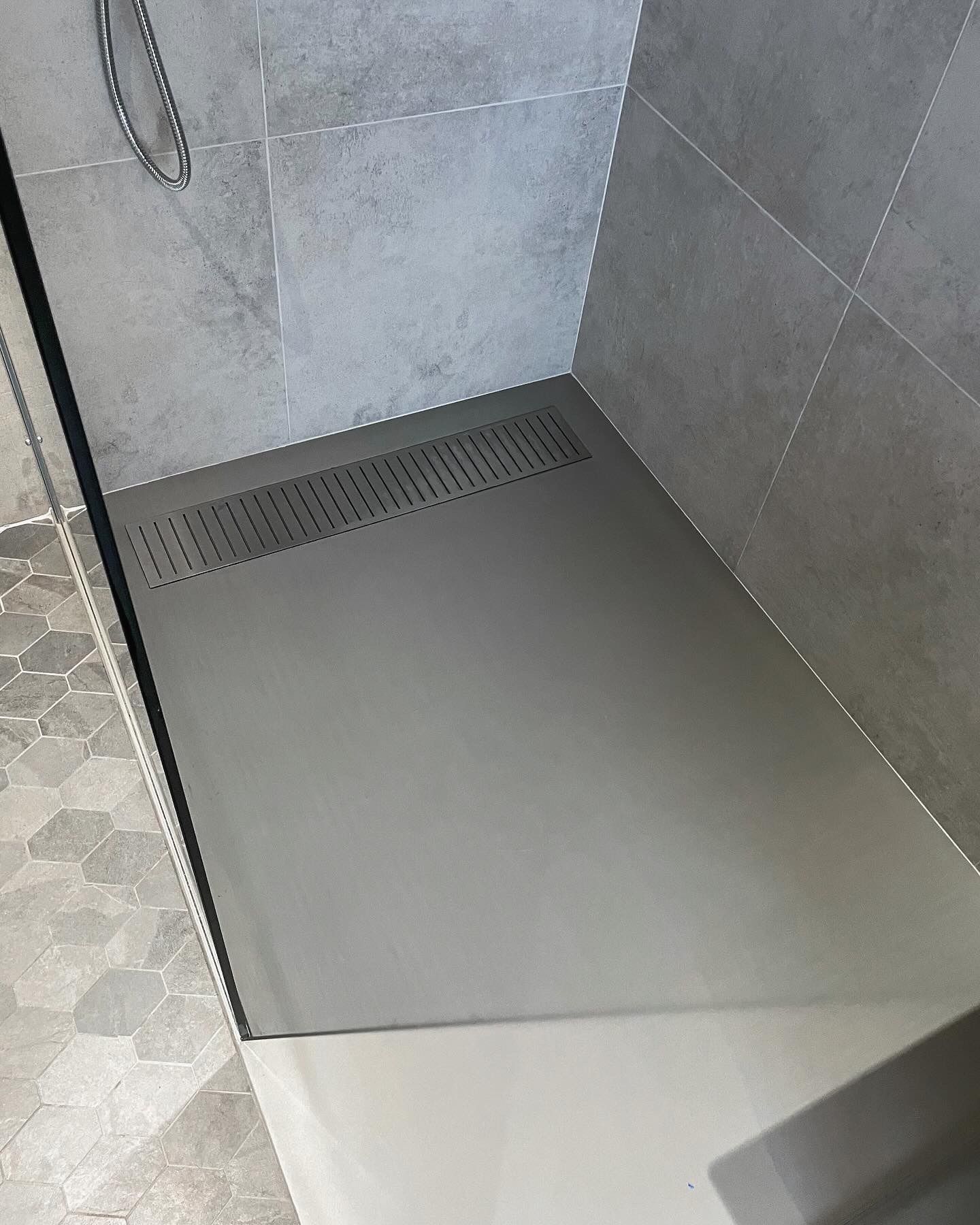 Douche avec murs et sol carrelés gris, drain le long de l'arrière.