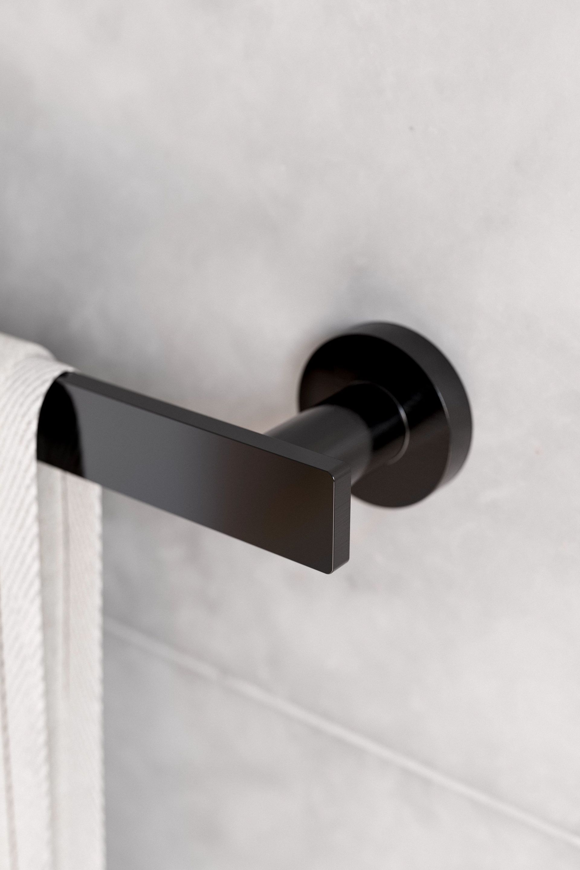 Barre porte-serviettes noire tenant une serviette blanche contre un mur carrelé gris clair.