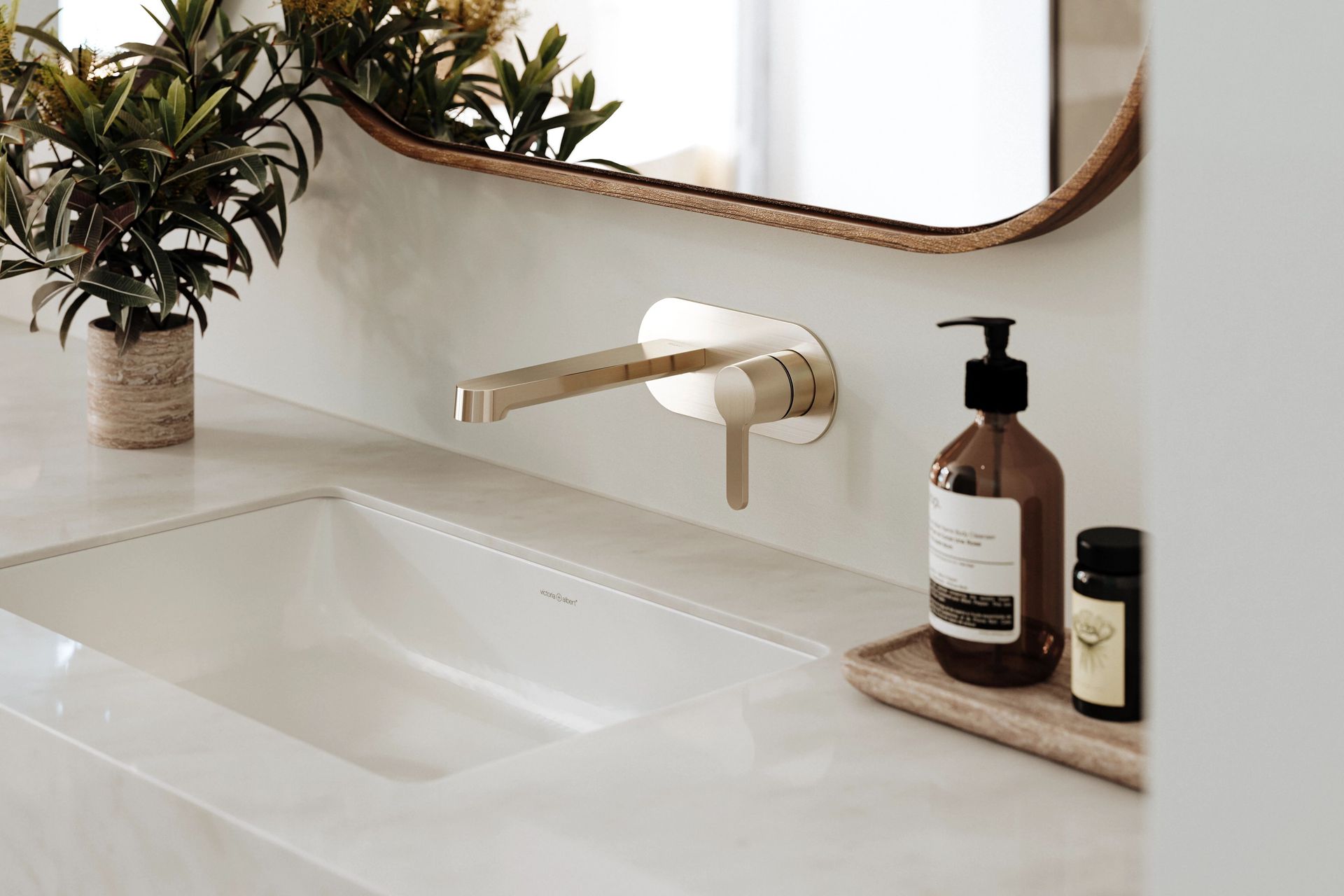 Lavabo de salle de bain avec robinet doré, comptoir blanc, miroir et objets décoratifs.