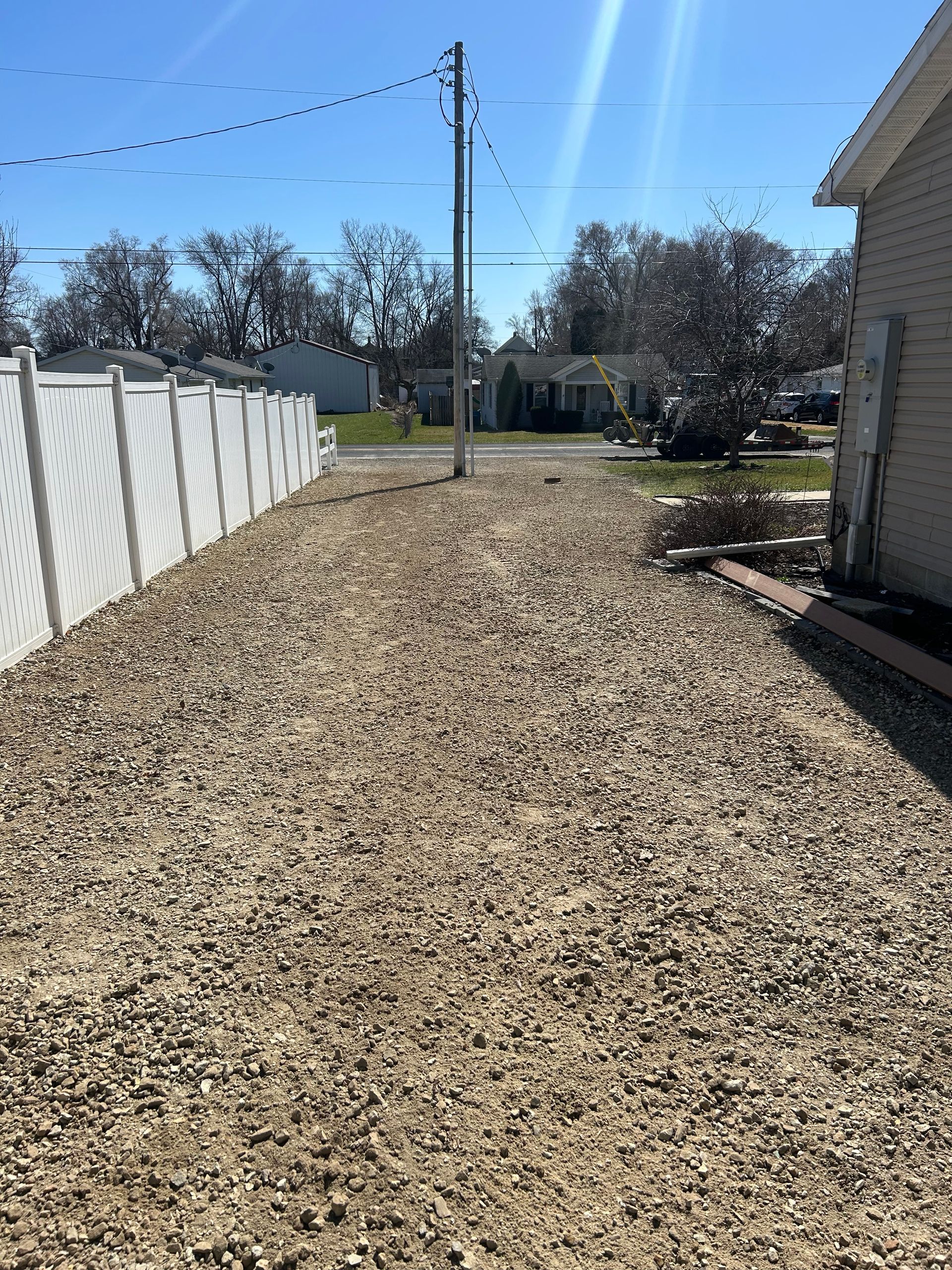 A gravel driveway with a white fence in the background
