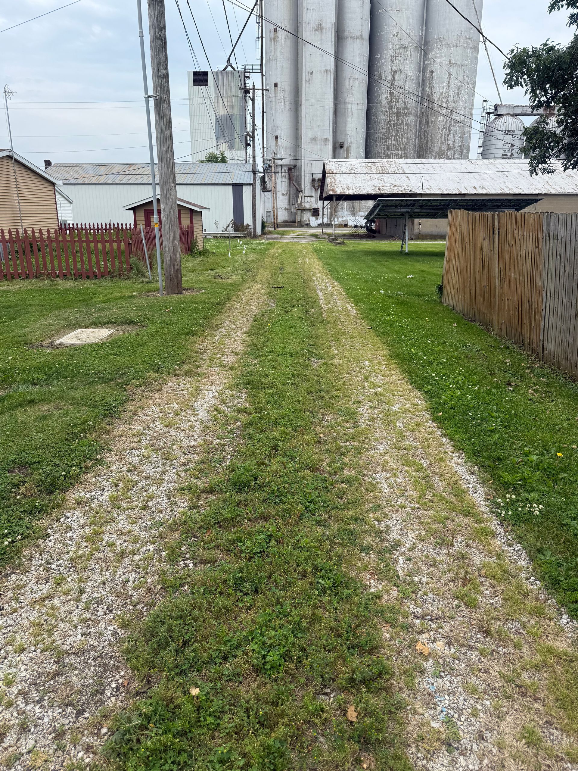 A gravel road going through a grassy field with a silo in the background.