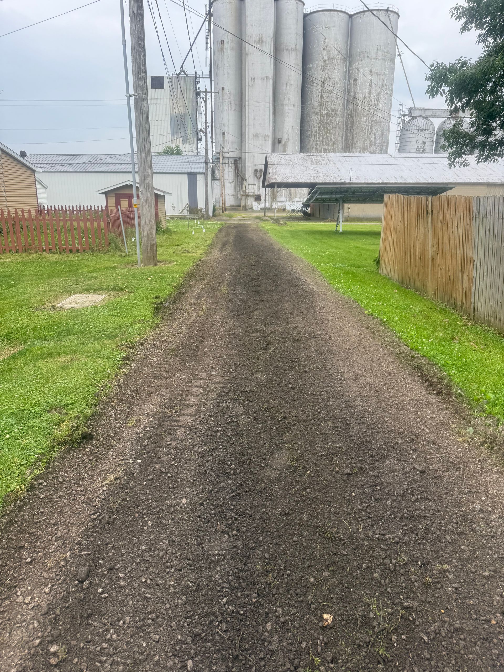 A dirt road leading to a farm with silos in the background.