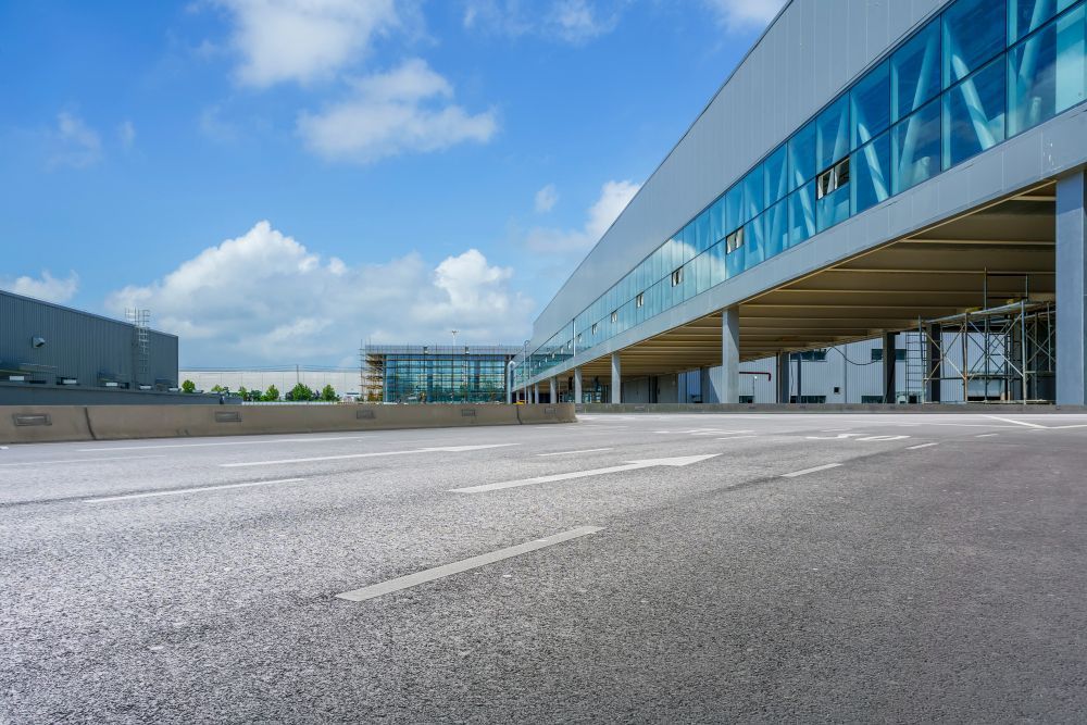 Terminal aeroportuário moderno com passarela suspensa de vidro azul e pátio de asfalto vazio sob um céu claro.