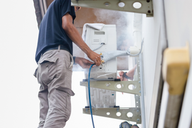 A man is working on an air conditioner on the side of a building.