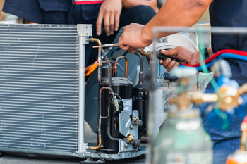 A man is working on an air conditioner outside of a brick building.