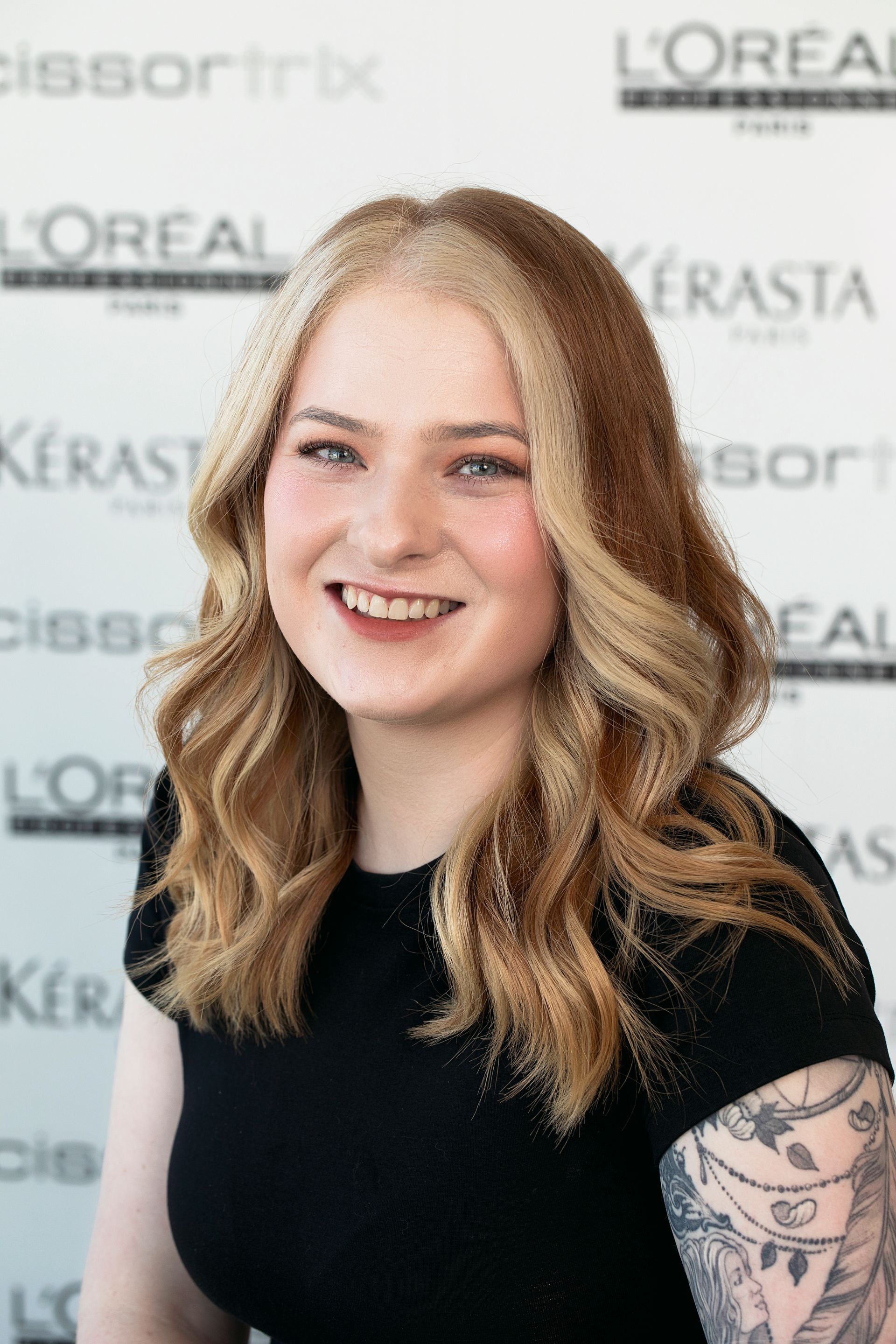 A woman with red hair is smiling in front of a wall with kerastase written on it