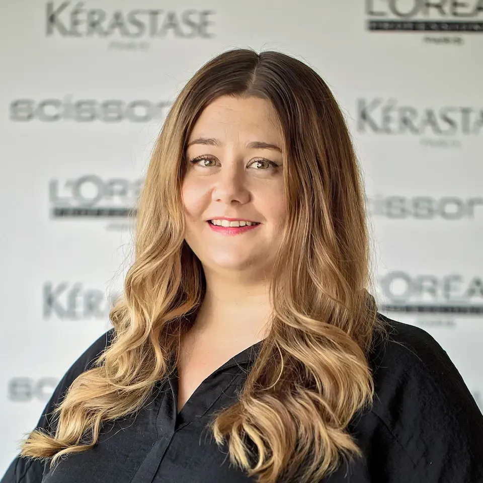 A woman with long hair is smiling in front of a loreal sign.