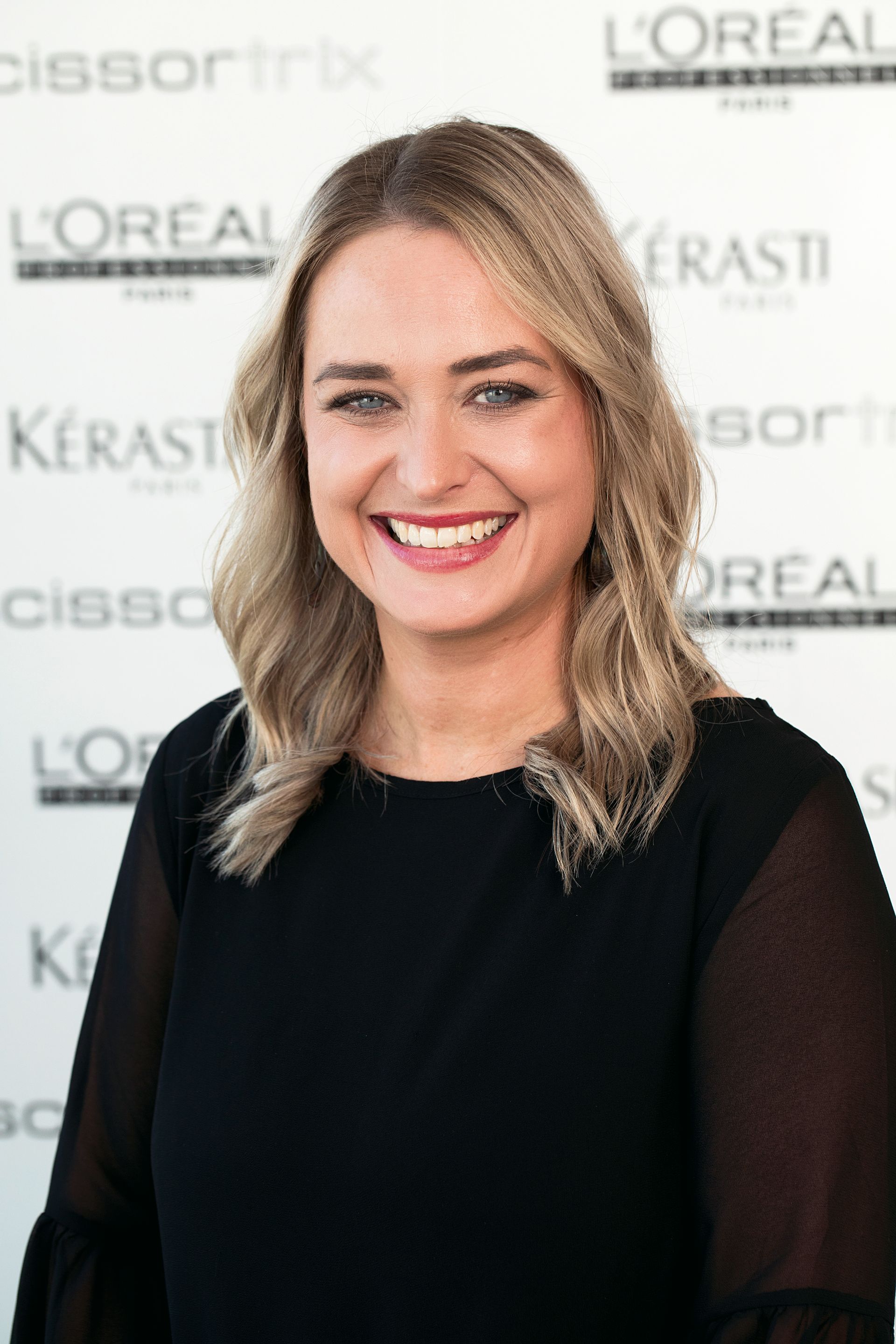 A woman is smiling in front of a wall that says l' oreal