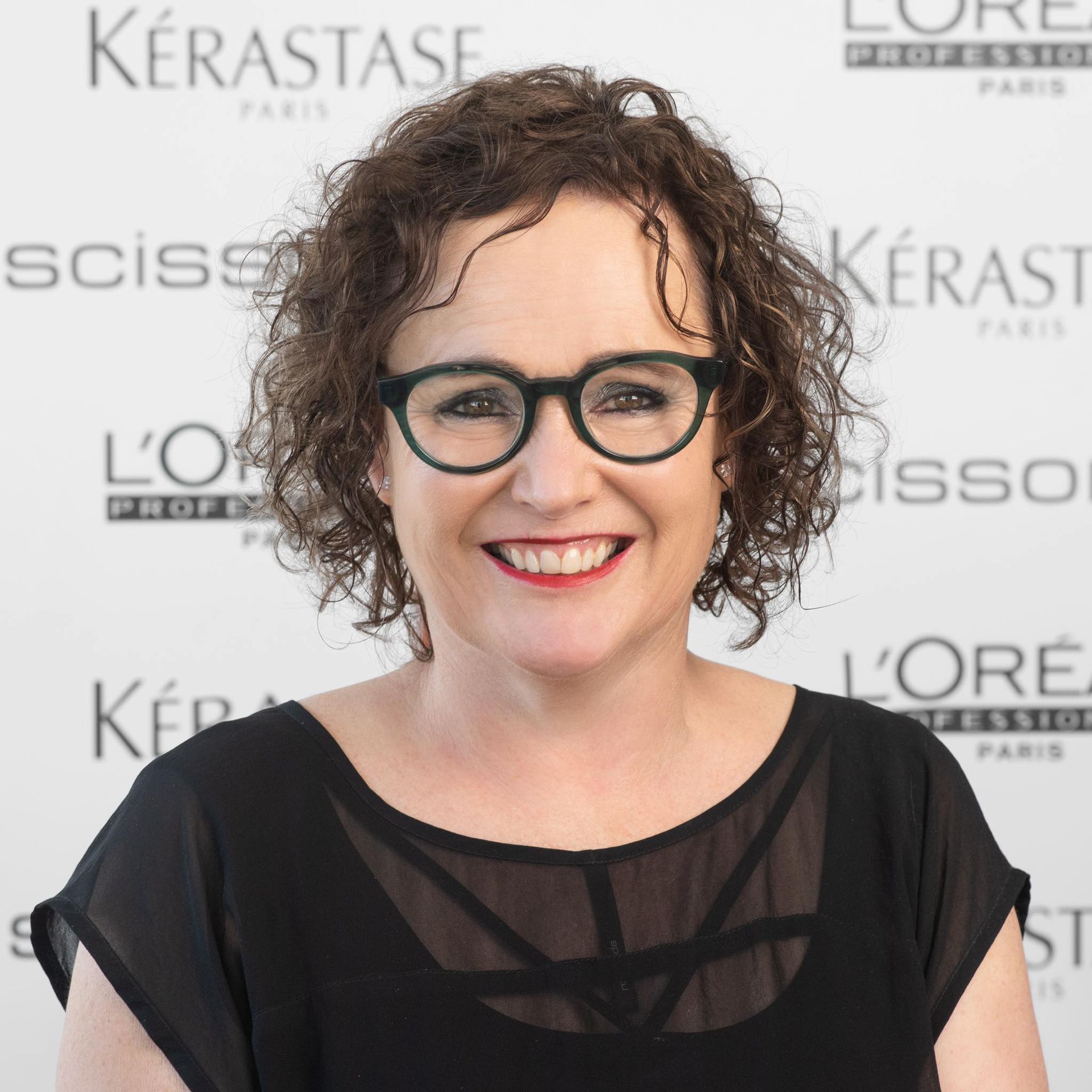 A woman wearing glasses and a black jacket is smiling for the camera.