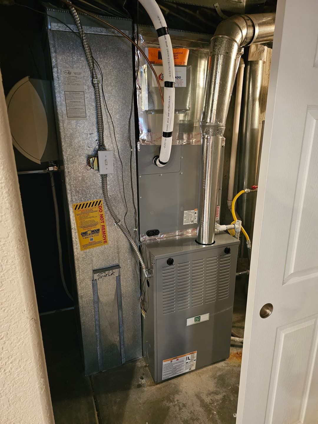 Furnace unit in a utility room with ductwork, gas line, and electrical components. Gray and silver tones dominate.