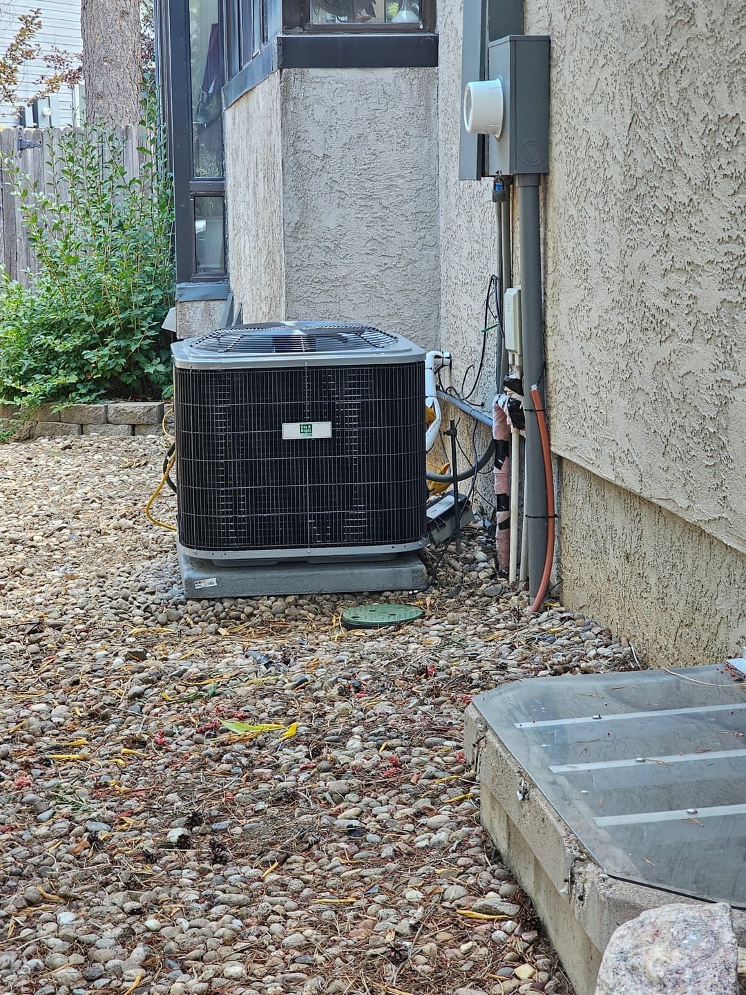 Central AC unit next to a stucco house, surrounded by gravel. Electrical components visible.
