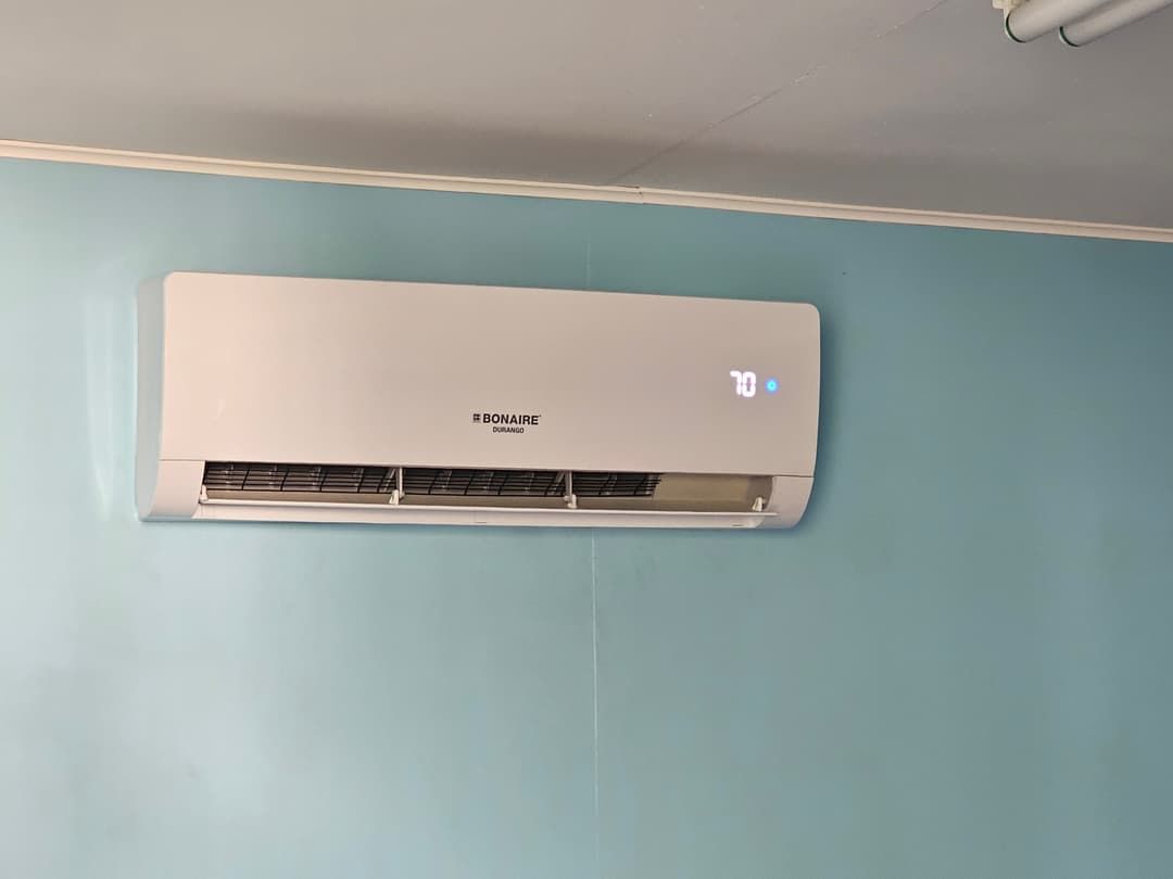 White wall-mounted air conditioner on a light blue wall. The temperature is displayed digitally.