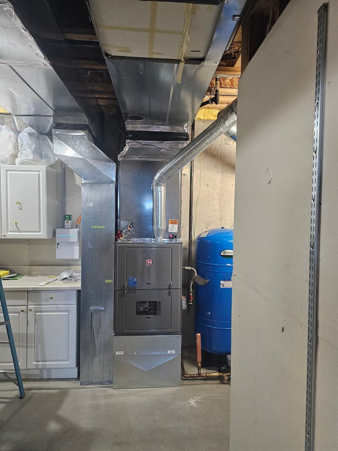 HVAC system in a basement with ductwork, a water tank, and a cabinet.