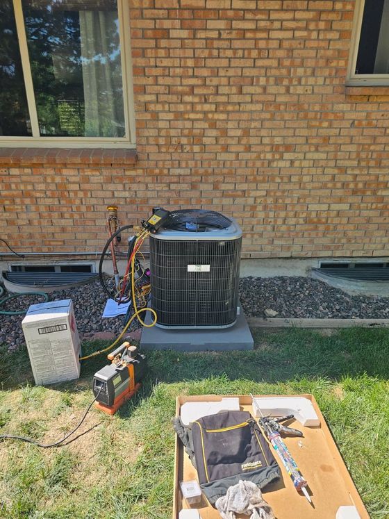 HVAC technician servicing an air conditioning unit on brick building, with tools and vacuum pump present.