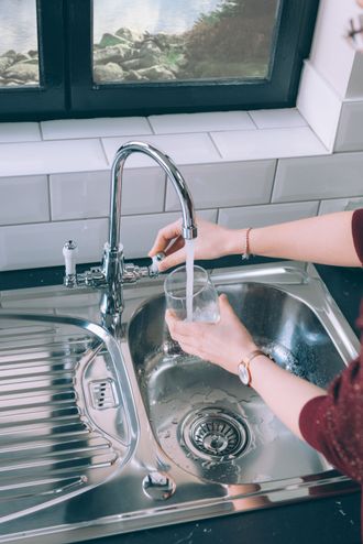 Woman filling a glass with water from a steel faucet