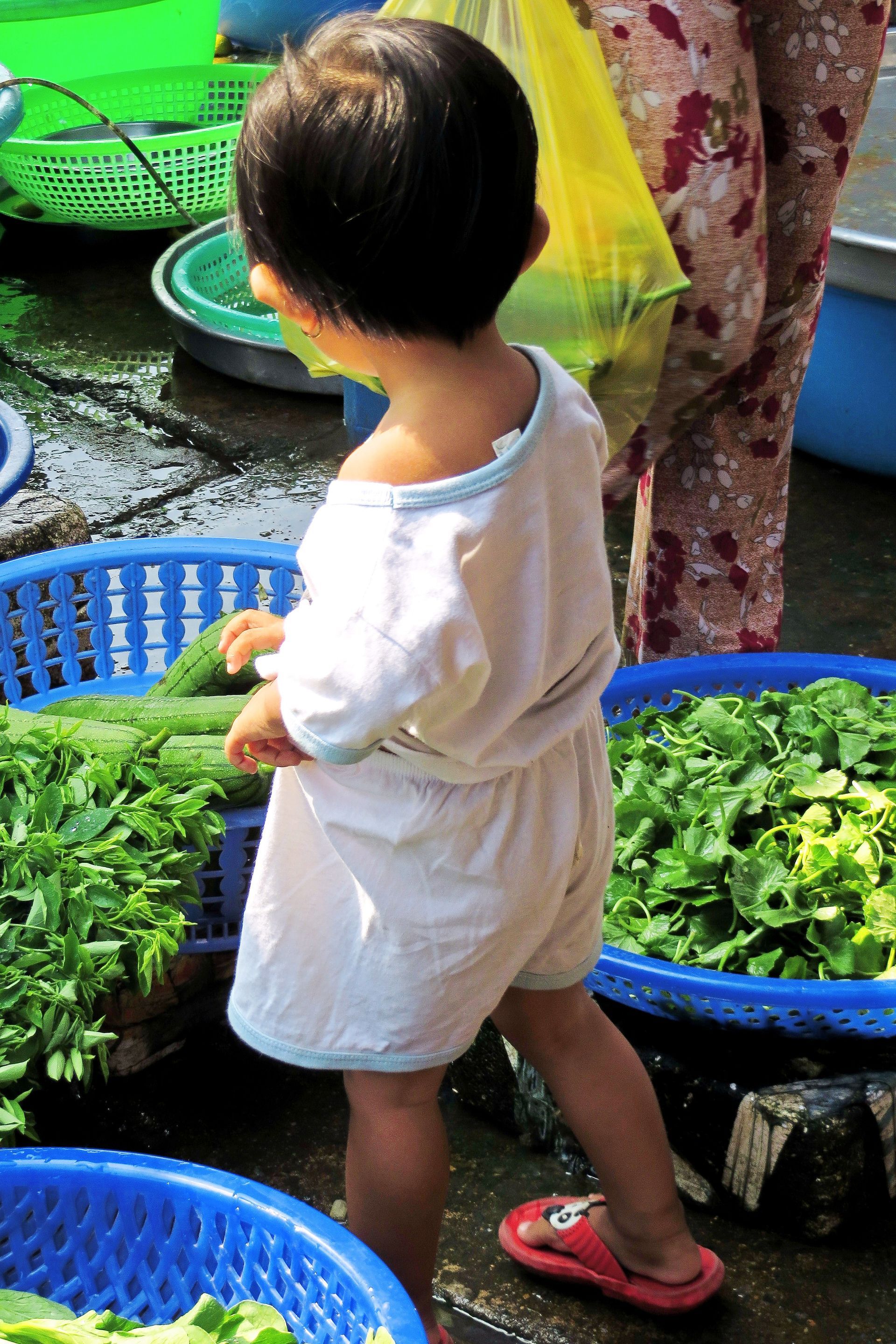 A little boy is standing in front of baskets of vegetables