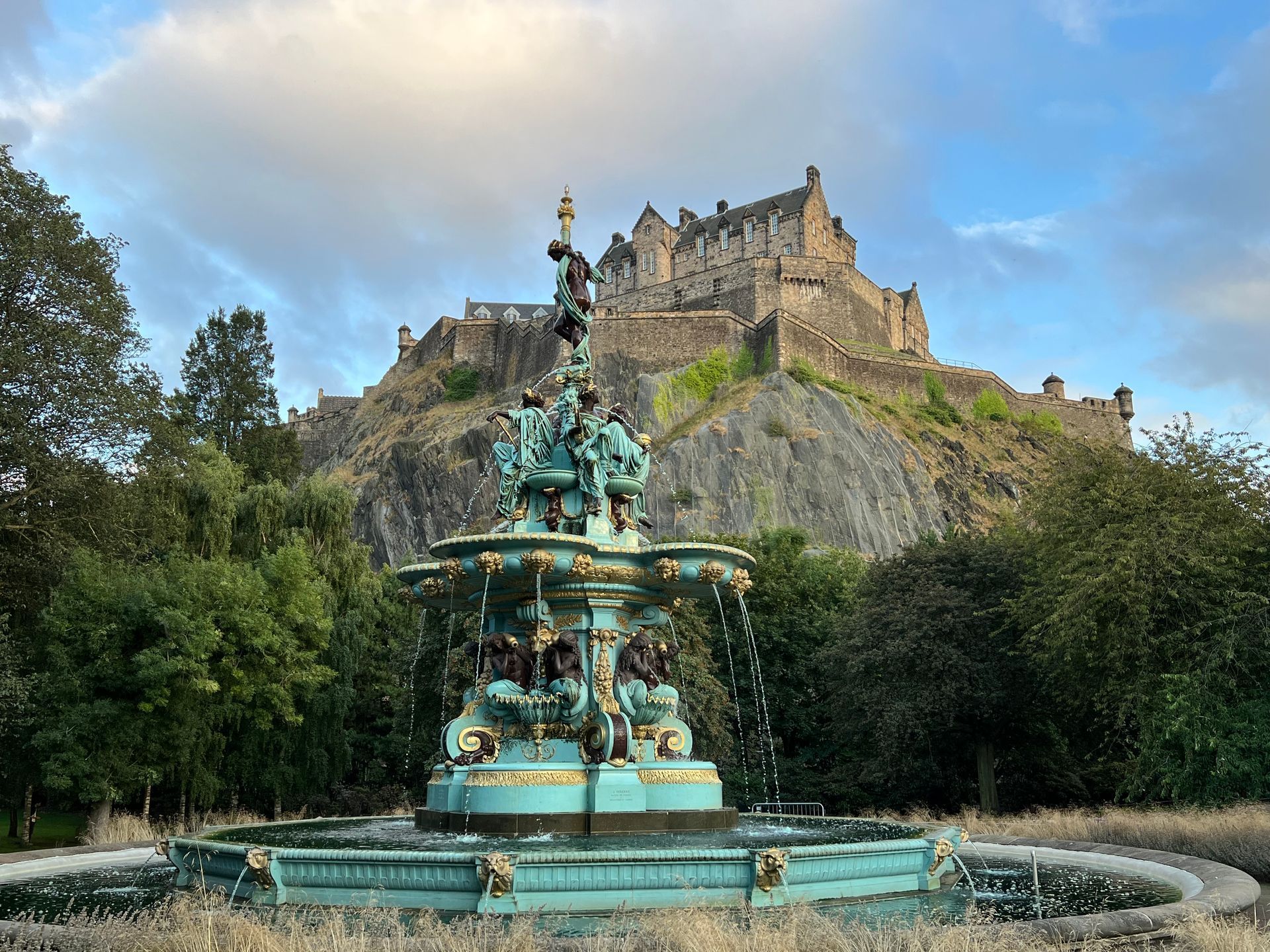 A fountain in front of a castle on top of a hill.