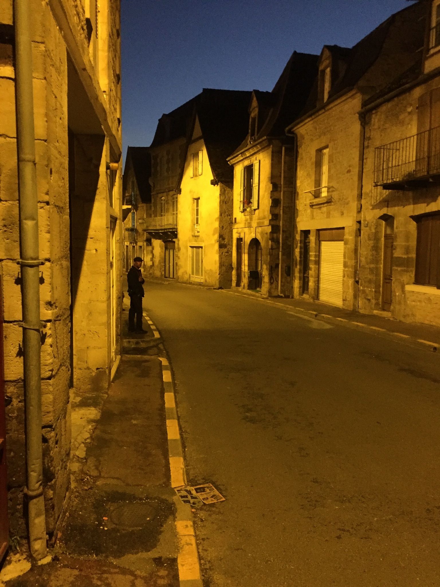 A narrow street with a man standing on the sidewalk at night