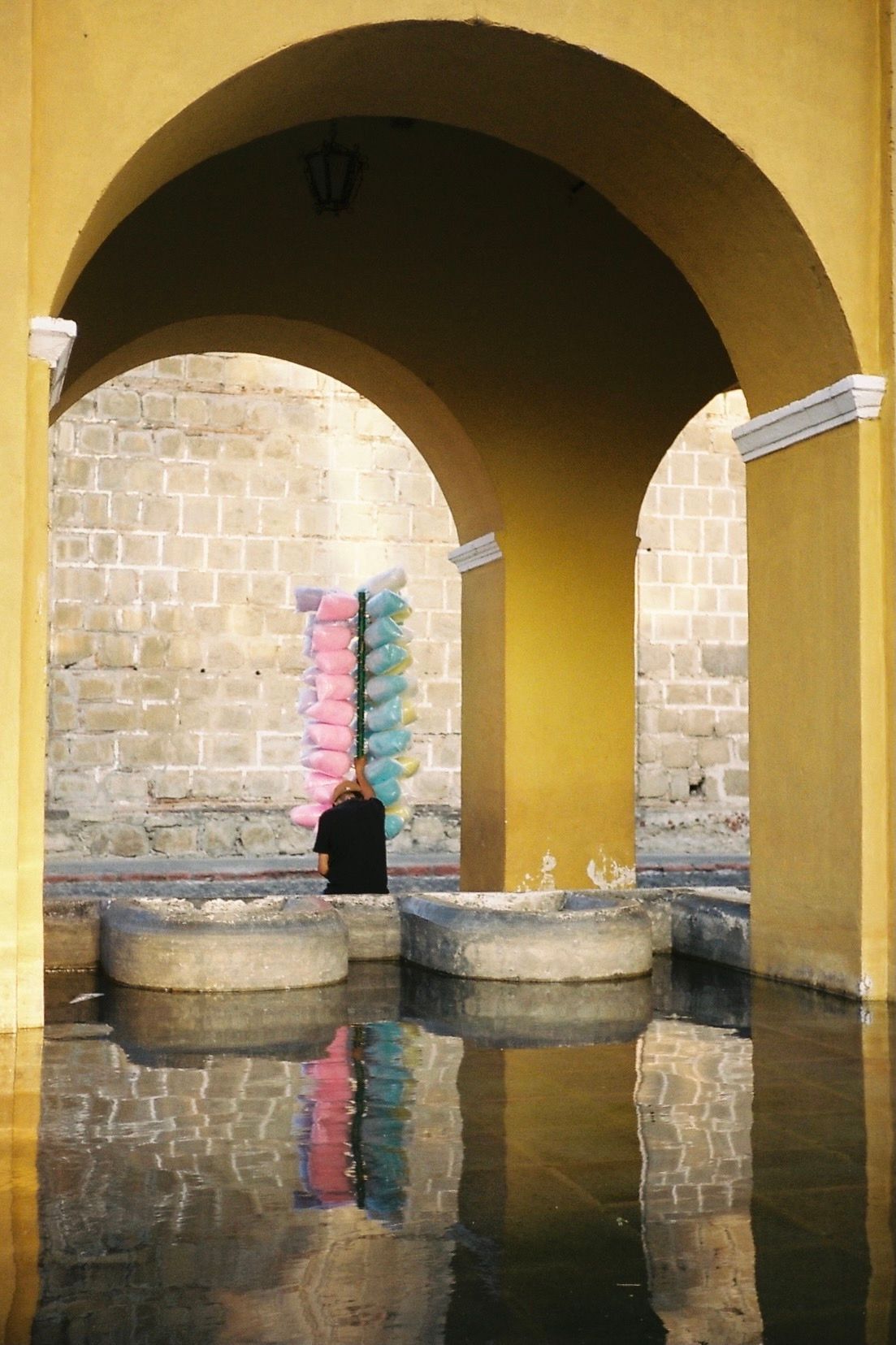 A man in a black shirt is standing under an archway with a bunch of cotton candy hanging from it